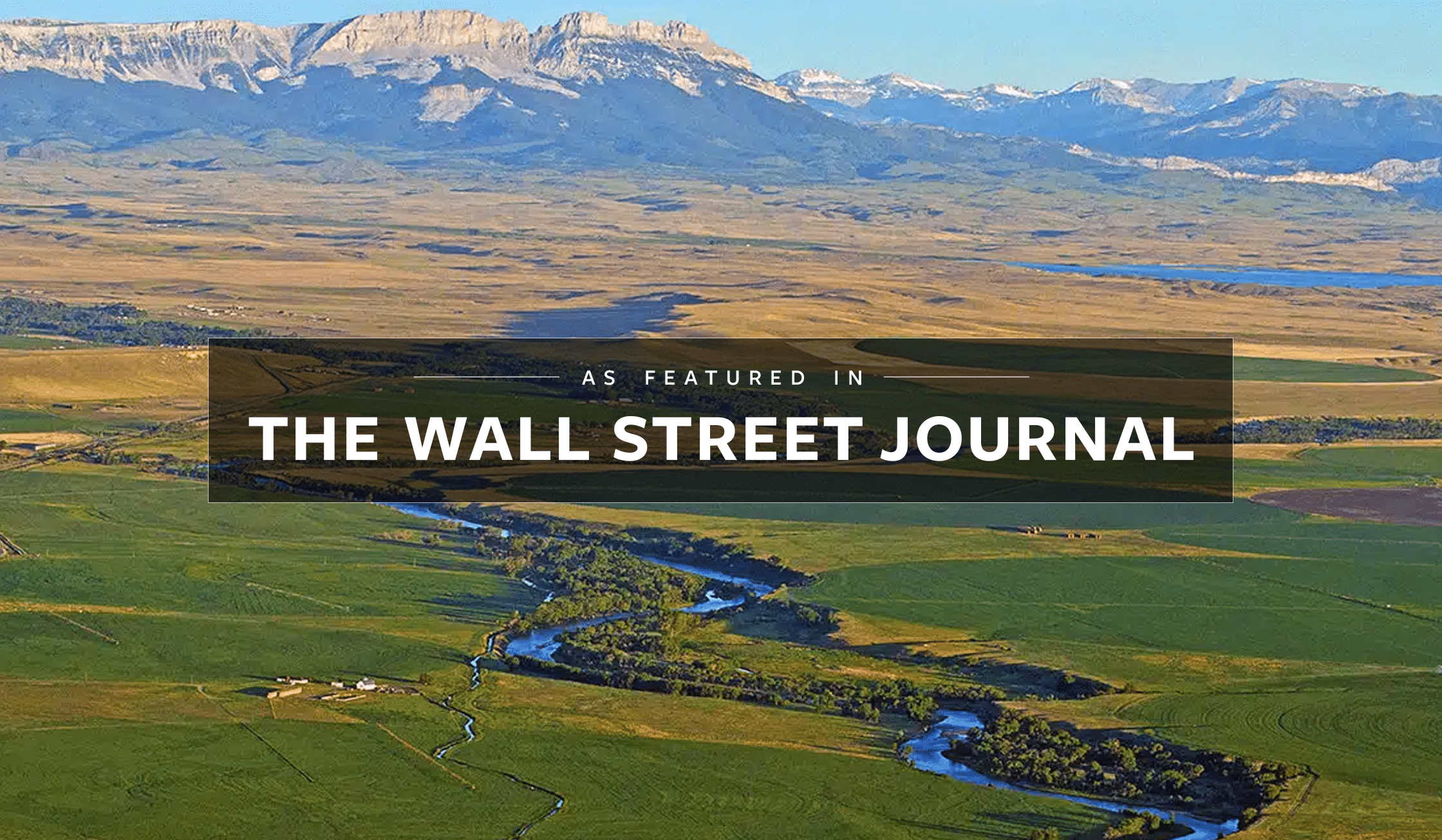 Aerial view of a green landscape with a winding river, fields, distant mountains, and open recreational land under a blue sky, overlaid with the text “As featured in THE WALL STREET JOURNAL.”.