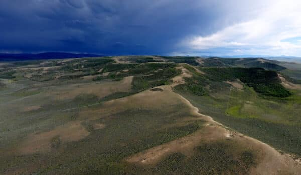 Aerial view of rolling hills and open plains on a cattle ranch, with dark storm clouds approaching from the left and sunny sky on the right, casting contrasting light over this picturesque recreational land.
