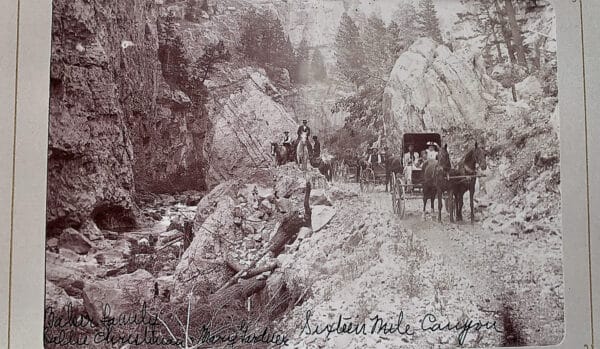 Black-and-white photo of a rocky canyon road with a horse-drawn carriage and several people. Tall cliffs and trees surround the scene, identified as Sixteen Mile Canyon—a striking glimpse of recreational land amidst natural beauty.