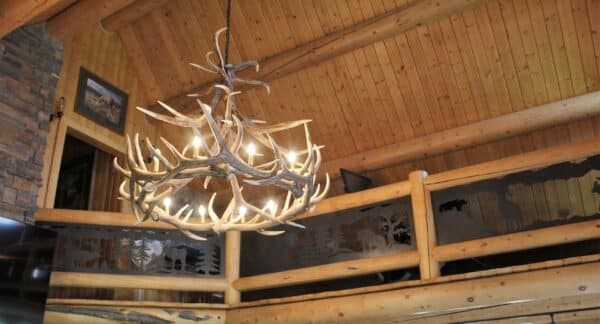 A rustic log cabin interior with a vaulted wooden ceiling, antler chandelier, and a loft railing decorated with nature-themed metal art—perfect for relaxing after a day on your hunting property or exploring expansive recreational land.