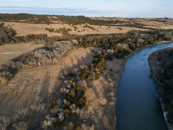 A winding river flows through a landscape of rolling hills and open grassland, dotted with scattered trees—ideal for a cattle ranch or hunting property under a clear sky.