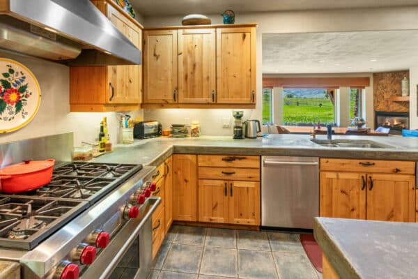 A cozy kitchen with wooden cabinets, stainless steel appliances, a gas stove with red knobs, a double sink, and a window view of green fields and mountains—perfect for enjoying scenic land for sale or nearby recreational land.