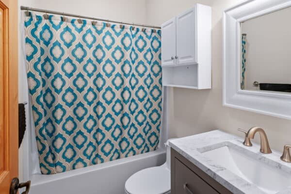 A bathroom with a white bathtub, a blue and white patterned shower curtain, a white vanity with marble countertop, a wall-mounted cabinet, and a framed mirror above the sink—perfect for relaxing after exploring your recreational land.