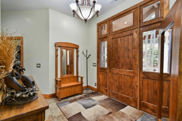 A spacious entryway with wooden double doors, a matching bench and mirrors, a coat rack, light fixture, decorative vase on a table, and a patterned rug on tiled floor welcomes you to this inviting hunting property.