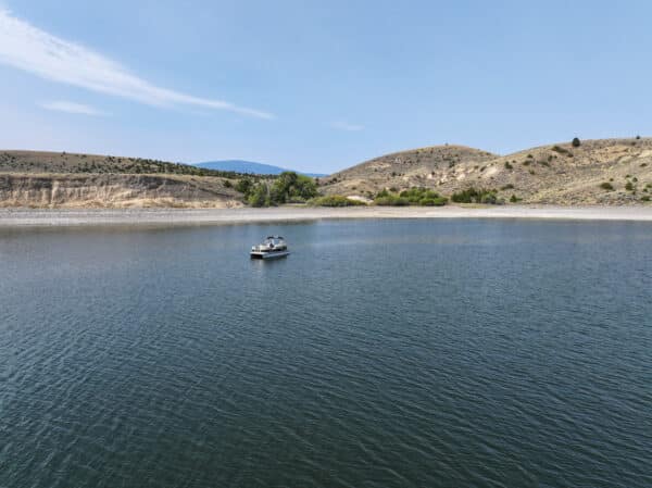 A small boat floats on a calm lake surrounded by gently sloping, dry hills and sparse vegetation—perfect recreational land under a clear blue sky.