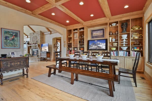 A dining room with a wooden table and benches, built-in shelves filled with dishes and decor, a rug under the table, and a view into a cozy living room—perfect for gatherings on recreational land or after a day at your hunting property.